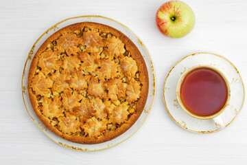 Homemade apple and cinnamon pie and cup of tea on white wooden table. Top view.