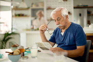 Senior man reading newspaper while having breakfast at home.