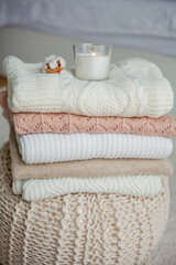 Fototapeta na wymiar A stack of knitted sweaters, cotton, a candle. Women's sweaters lie on the ottoman. Cozy autumn clothes.