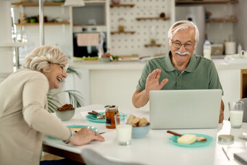 Obraz premium Happy senior couple making video call over laptop while having breakfast at home.