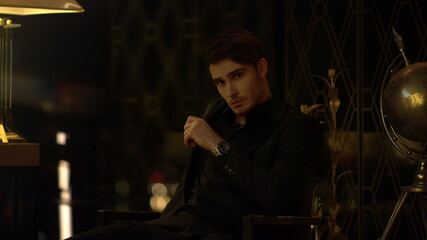 Sexy guy waiting for someone in dark room. Confident man looking around indoors.