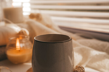A cozy and warm hygge concept with white sweaters, candles, a cup, a garland on the windowsill. Autumn trends