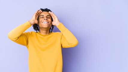 Young black man wearing rasta hairstyle laughs joyfully keeping hands on head. Happiness concept.