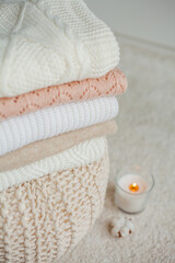 A stack of knitted sweaters, cotton, a candle. Women's sweaters lie on the ottoman. Cozy autumn clothes.