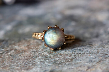 Brass metal decorative ring with natural mineral labradorite gemstone on grey neutral rocky background