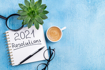 New year resolutions 2021 on desk. 2021 goals with notebook, coffee cup and eyeglasses on blue...
