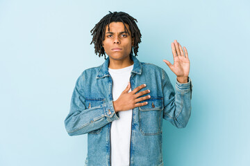 Young black man wearing a jeans jacket taking an oath, putting hand on chest.