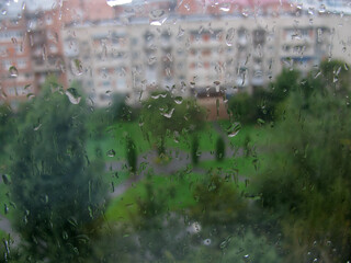 raindrops on the glass. Outside the window is a high-rise building and trees.