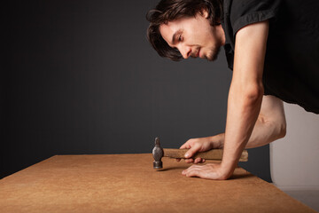 A man hammers nails into a cupboard. The back wall of the cupboard is made of thick cardboard.