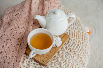 A mug of hot tea, a teapot, knitted sweater, a wooden stand on an ottoman. Cozy autumn. Winter breakfast. Cotton.