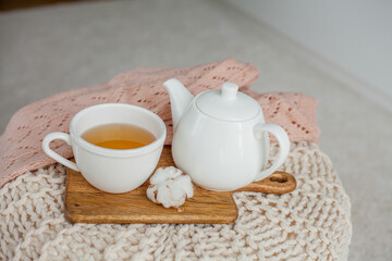 Fototapeta na wymiar A mug of hot tea, a teapot, knitted sweater, a wooden stand on an ottoman. Cozy autumn. Winter breakfast. Cotton.