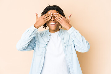 Young african american rasta man covers eyes with hands, smiles broadly waiting for a surprise.