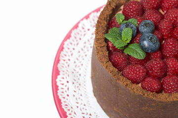 No-bake chocolate cake with cream cheese. Garnished with raspberries, blueberries and mint leaves. On a white surface.