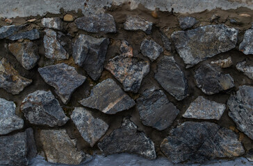 gray blue textured stone in rough cement in a sloppy wall with cracks, the work of builders, a rustic fence
