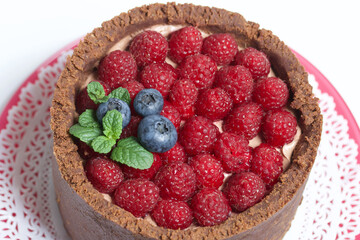 No-bake chocolate cake with cream cheese. Garnished with raspberries, blueberries and mint leaves. On a white surface.
