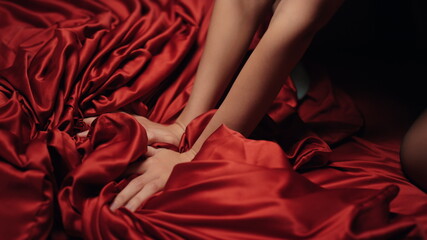 Woman hands holding red satin sheet on bed. Unknown girl having moment pleasure.