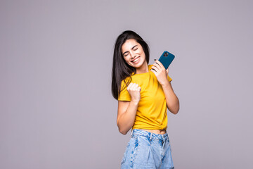 Happy young woman clenching her fists in winner gesture, looking at camera, isolated over gray...