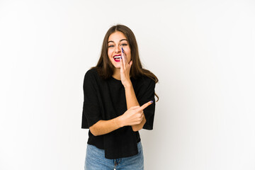 Young caucasian woman isolated on white background saying a gossip, pointing to side reporting something.