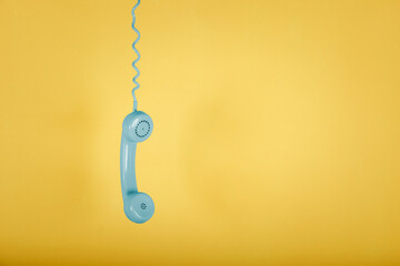 blue vintage telephone hanging on yellow background