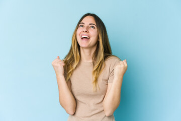 Young caucasian woman isolated on blue background raising fist after a victory, winner concept.