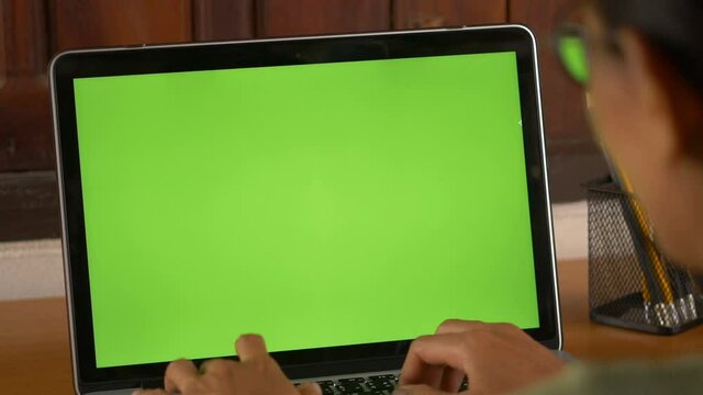 Over the shoulder shot of woman, using finger with keyboard for typing touch. computer laptop with blank green screen chroma key.