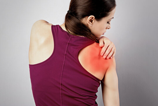 Young strong sporty woman suffering from pain in shoulder in sport wear. Touching the hand. Sports exercising injury. Closeup portrait with highlighted in red and empty space. Back view.