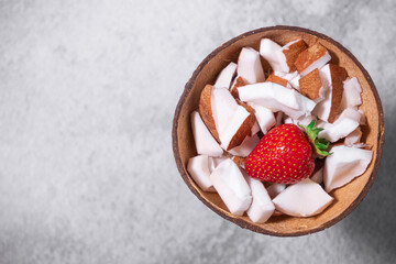 A bowl of coconut pieces and strawberry on concrete background. Coconut ingredient on plate. Vegan...