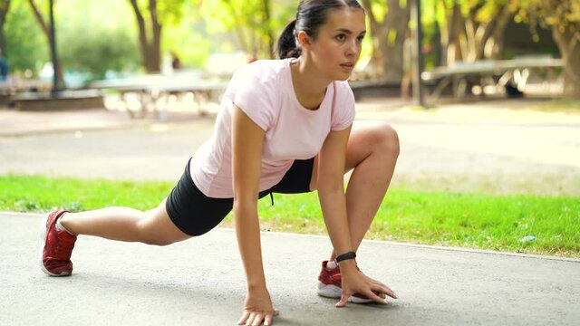 Young woman in sportswear doing low stretching of legs before running in park. Athletic female warming up outside. Concept of sport