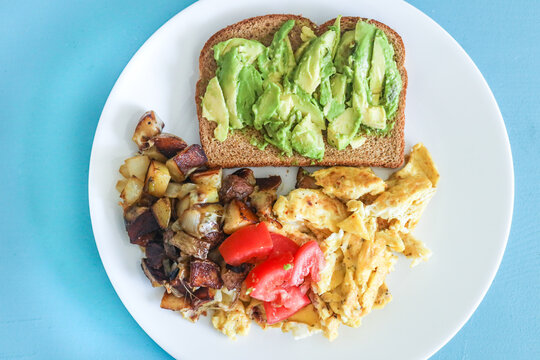 Balanced healthy vegetarian breakfast avocado toast, scrambled eggs, potatoes and tomato.
