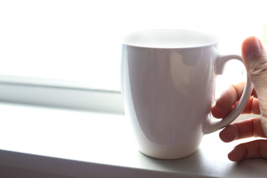 Coffee mug in hand on a bright white windowsill