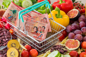 Shopping basket with Bolivian money, around food products, vegetables and fruits.  The concept of...
