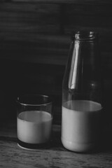 Black and white photo of half a bottle of fresh milk and poured in a glass a wooden background