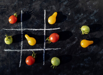 Multi-colored cherry tomatoes laid out on a dark background in the cells, drawn with chalk. Didactic game. Background with food.