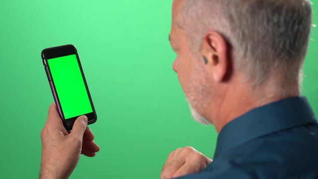 Green screen background with tablet also having green screen of man talking to someone over video call on his phone and smiling and coughing.