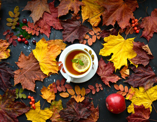 Autumn background with dry maple and rowan leaves, apple and a cup of tea with lemon .. Poster, banner.