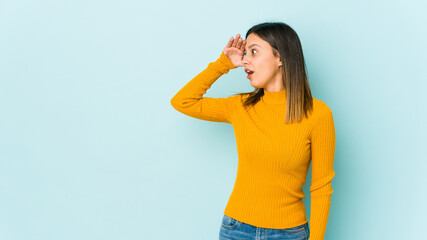 Young woman isolated on blue background looking far away keeping hand on forehead.