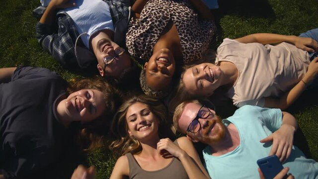 Top view of diverse team of friends relaxing in park lying on grass in circle