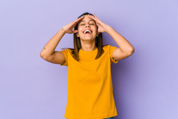 Young woman isolated on purple background laughs joyfully keeping hands on head. Happiness concept.