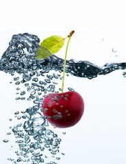 A cherry with stem and leaf underwater in sparkling water