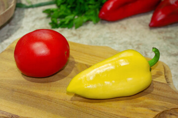 Red tomato, yellow bell pepper on a wooden board. Parsley, cilantro and two red peppers in the back. Ingredient for cooking