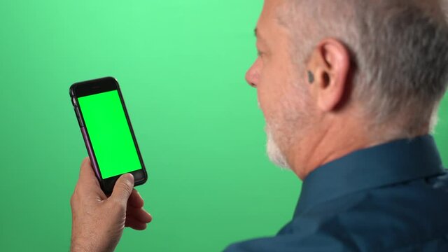 Green screen background with tablet also having green screen of man talking to someone serious over video call on his phone.