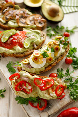Vegetarian sourdough bread sandwiches with avocado paste and various toppings, focus on the sandwich inside with boiled eggs and green olives close up view