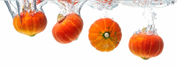Four orange pumpkins splashing into crystal clear water. Product isolated on white background.