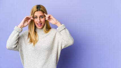 Young blonde woman isolated on purple background receiving a pleasant surprise, excited and raising hands.