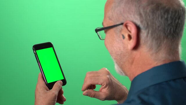 Green screen background with tablet also having green screen of man talking to someone over video call on his phone and smiling waving hello.