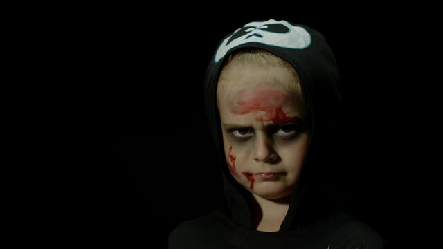 Halloween, angry girl with blood makeup on face. Kid dressed as scary skeleton, posing, making faces