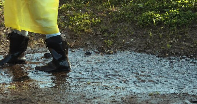 woman in a yellow raincoat and rubber boots jumping through puddles
