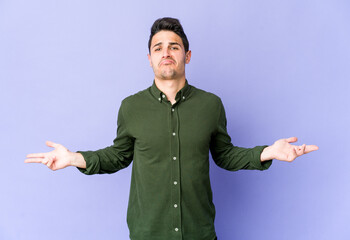 Young caucasian man isolated on purple background doubting and shrugging shoulders in questioning gesture.