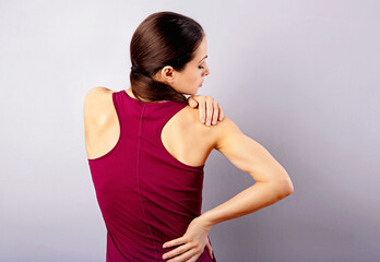 Young strong sporty woman looking on the shoulder with pain in sport clothing. Touching and massaging the hands. Sports exercising injury. Closeup portrait on purple background