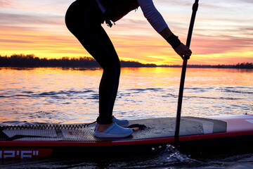 Legs of a girl on stand up paddle board (SUP) with a paddle at winter river at sunset